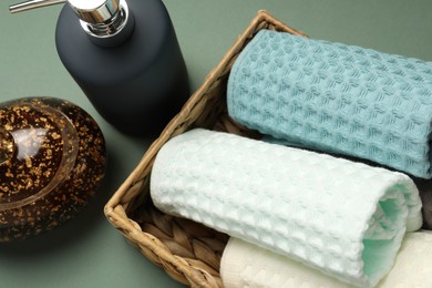 Photo of Clean waffle towels in wicker basket and cosmetic products on green background, above view
