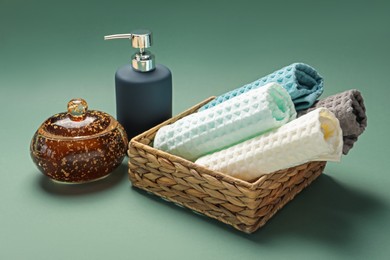 Photo of Clean waffle towels in wicker basket and cosmetic products on green background