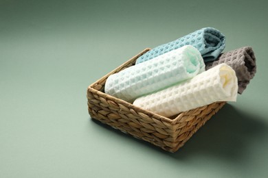 Photo of Clean waffle towels in wicker basket on green background, closeup. Space for text