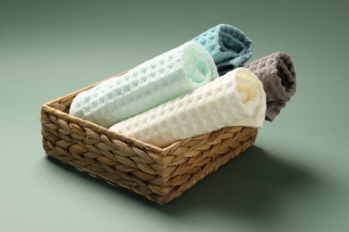 Photo of Clean waffle towels in wicker basket on green background, closeup