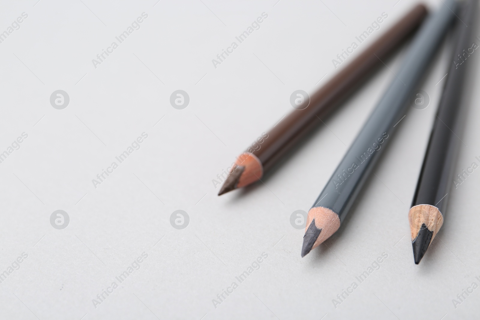 Three different eyebrow pencils on light background, closeup. Space for text Photo of Three different eyebrow pencils on light background, closeup. Space for text