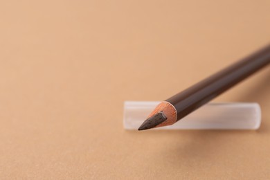 Photo of Brown eyebrow pencil on beige background, closeup. Space for text