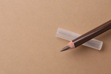 Photo of Brown eyebrow pencil on beige background, top view. Space for text