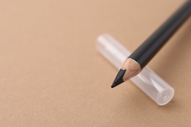 Photo of Black eyebrow pencil on beige background, closeup. Space for text