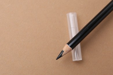 Photo of Black eyebrow pencil on beige background, top view. Space for text
