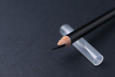 Photo of Black eyebrow pencil on dark background, closeup. Space for text