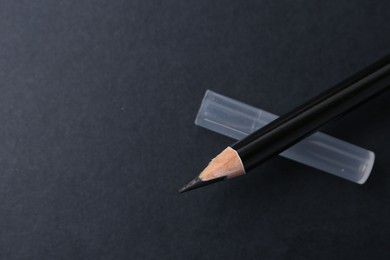 Photo of Black eyebrow pencil on dark background, top view. Space for text