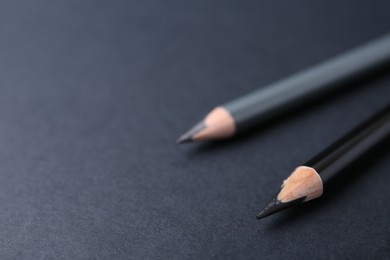 Photo of Two different eyebrow pencils on dark background, closeup. Space for text