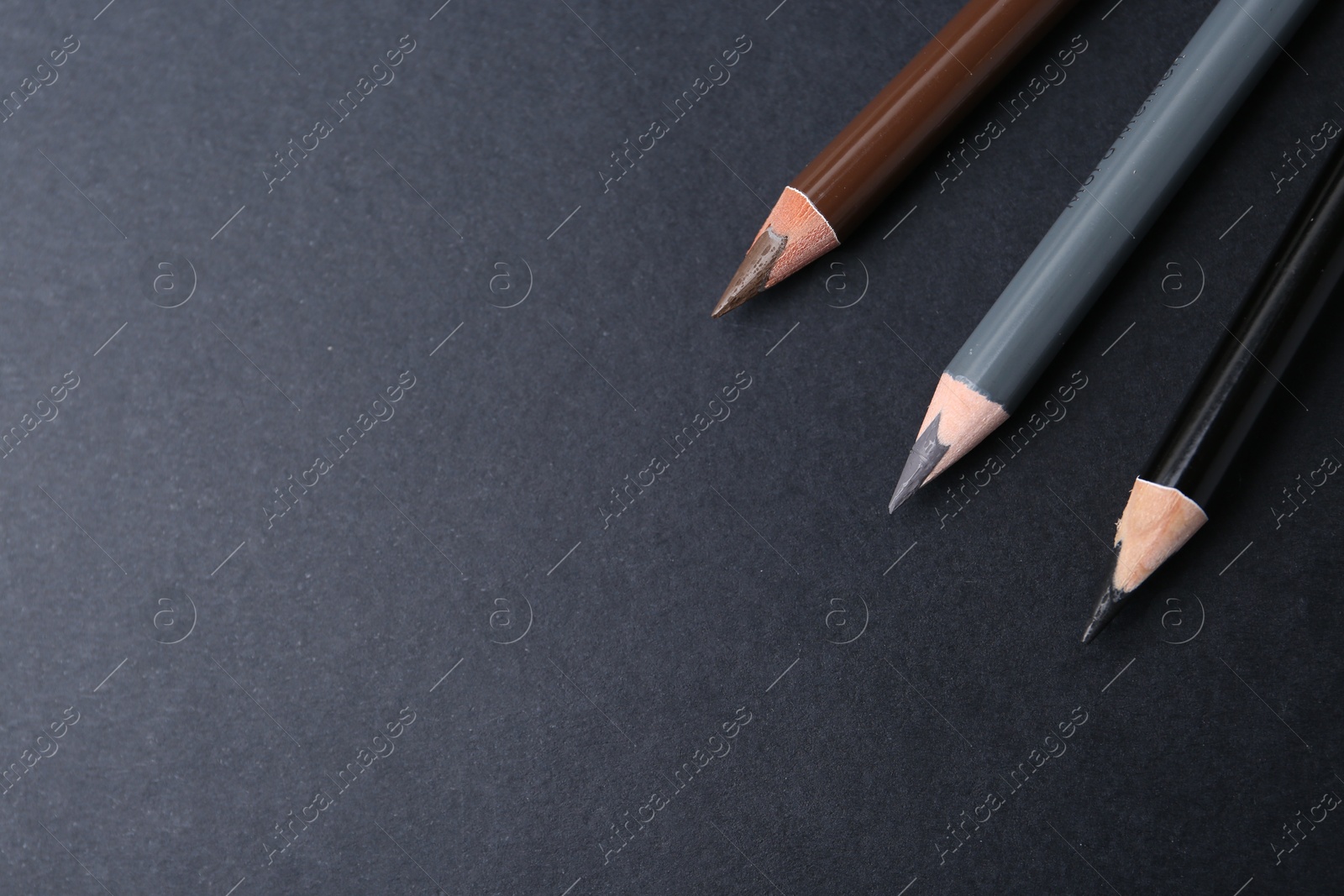 Three different eyebrow pencils on dark background, top view. Space for text Photo of Three different eyebrow pencils on dark background, top view. Space for text