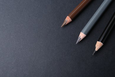 Photo of Three different eyebrow pencils on dark background, top view. Space for text