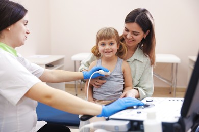 Photo of Sonographer conducting ultrasound examination of girl's heart. Mother and daughter having appointment with doctor in clinic