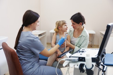 Photo of Sonographer conducting ultrasound examination of girl's heart. Mother and daughter having appointment with doctor in clinic