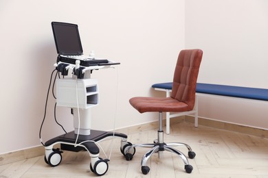 Photo of Modern ultrasound machine, chair and examination bed in clinic