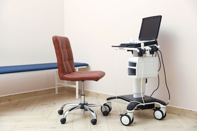 Photo of Modern ultrasound machine, chair and examination bed in clinic