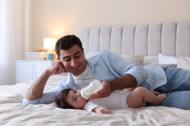 Photo of Father feeding his little baby with bottle on bed at home