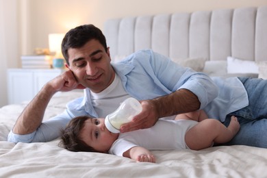Photo of Father feeding his little baby with bottle on bed at home