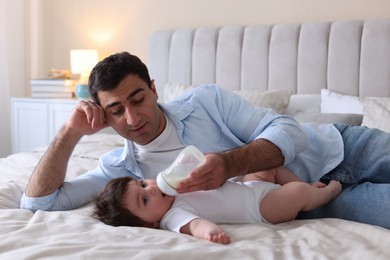 Photo of Father feeding his little baby with bottle on bed at home