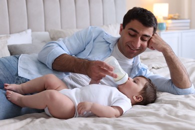 Photo of Father feeding his little baby with bottle on bed at home