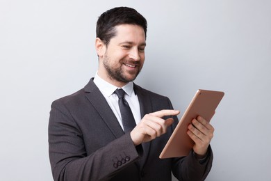Photo of Smiling businessman using tablet on light grey background