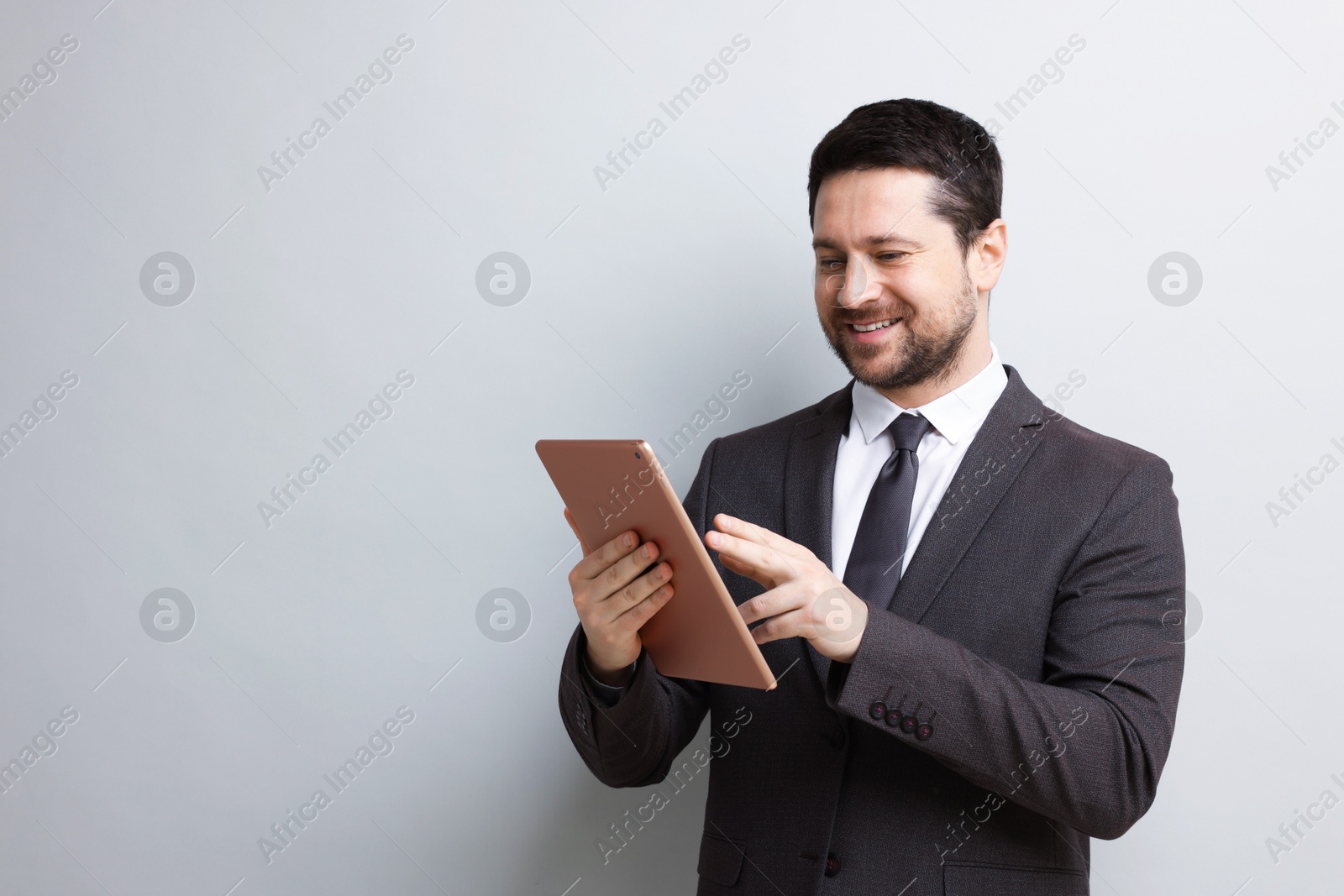 Smiling businessman using tablet on light grey background. Space for text Photo of Smiling businessman using tablet on light grey background. Space for text