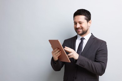 Photo of Smiling businessman using tablet on light grey background. Space for text