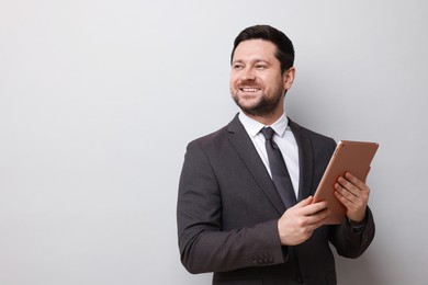 Photo of Smiling businessman with tablet on light grey background. Space for text