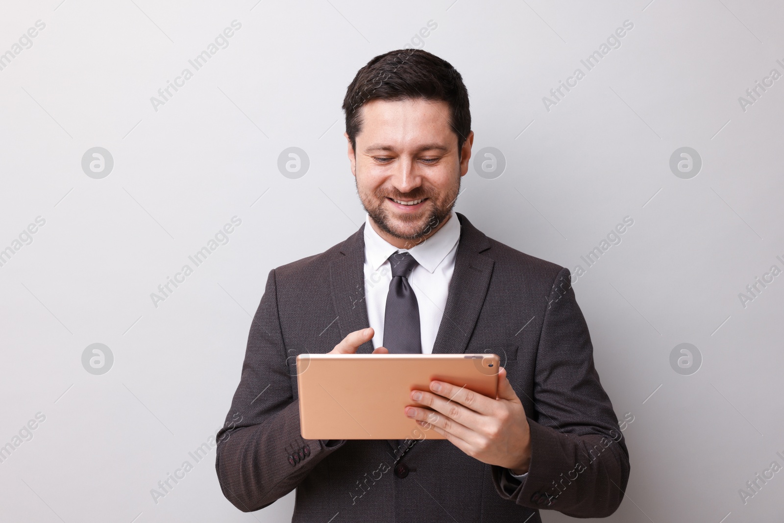Smiling businessman using tablet on light grey background Photo of Smiling businessman using tablet on light grey background
