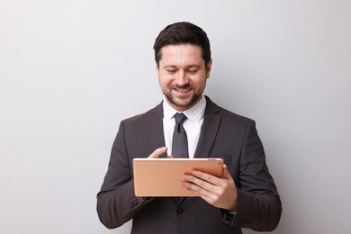 Photo of Smiling businessman using tablet on light grey background