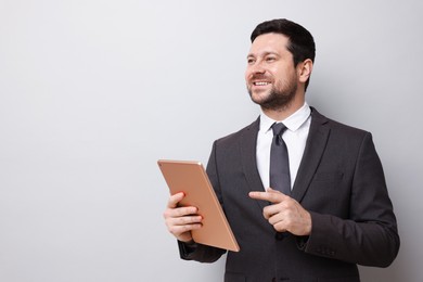 Photo of Smiling businessman with tablet on light grey background. Space for text