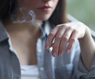 Photo of Woman smoking cigarette indoors, selective focus. Bad habit