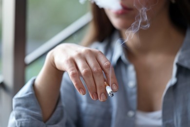 Photo of Woman smoking cigarette indoors, selective focus. Bad habit