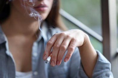 Photo of Woman smoking cigarette indoors, selective focus. Bad habit