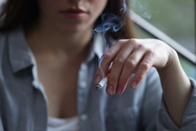 Photo of Woman smoking cigarette indoors, selective focus. Bad habit