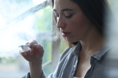 Photo of Woman smoking cigarette indoors, closeup. Bad habit