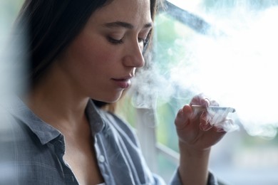 Photo of Woman smoking cigarette indoors, closeup. Bad habit