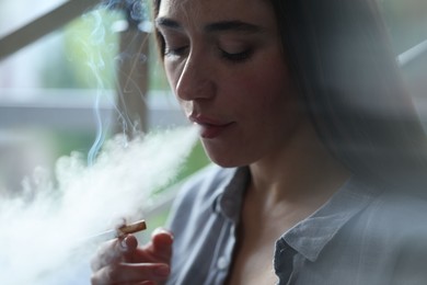 Photo of Woman smoking cigarette indoors, closeup. Bad habit