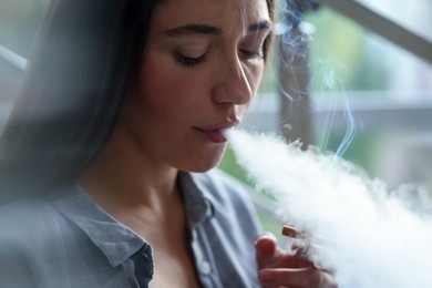 Photo of Woman smoking cigarette indoors, closeup. Bad habit