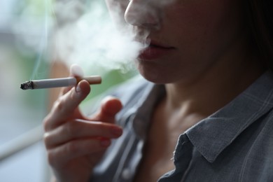 Photo of Woman smoking cigarette indoors, closeup. Bad habit