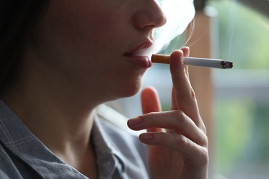 Photo of Woman smoking cigarette indoors, closeup. Bad habit
