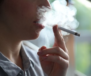 Photo of Woman smoking cigarette indoors, closeup. Bad habit