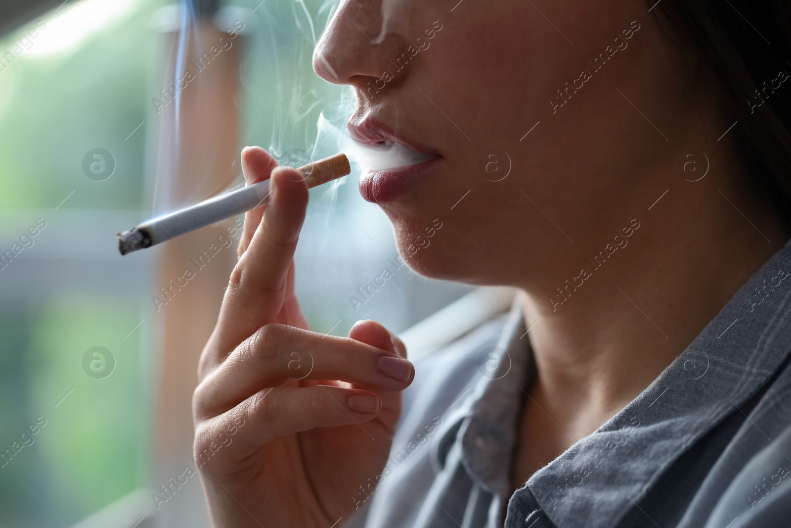 Woman smoking cigarette indoors, closeup. Bad habit Photo of Woman smoking cigarette indoors, closeup. Bad habit