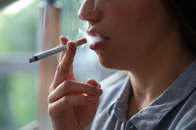 Photo of Woman smoking cigarette indoors, closeup. Bad habit