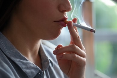 Photo of Woman smoking cigarette indoors, closeup. Bad habit