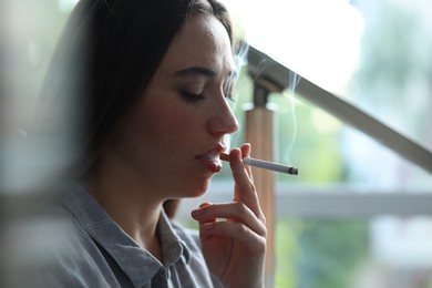 Photo of Woman smoking cigarette indoors, closeup. Bad habit