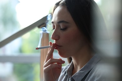 Photo of Woman smoking cigarette indoors, closeup. Bad habit