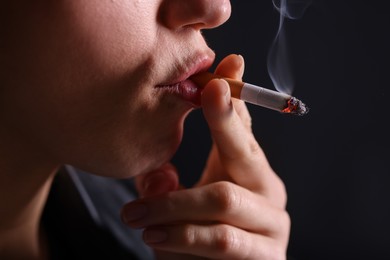 Photo of Woman smoking cigarette on black background, closeup