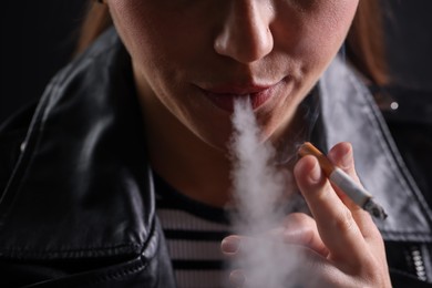 Photo of Woman smoking cigarette on black background, closeup