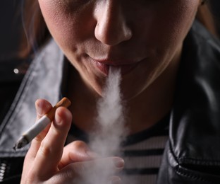 Photo of Woman smoking cigarette on black background, closeup