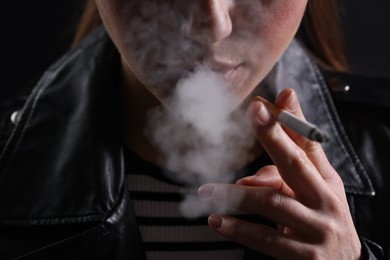 Photo of Woman smoking cigarette on black background, closeup