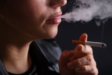 Photo of Woman smoking cigarette on black background, closeup